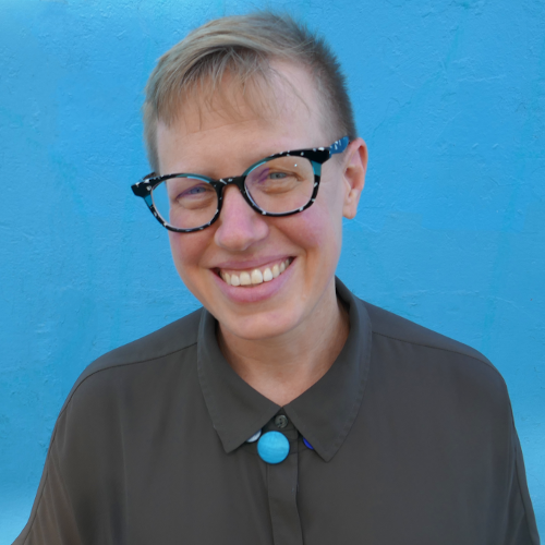 Headshot of Emily Drabinski; white woman in glasses standing in front of a blue background